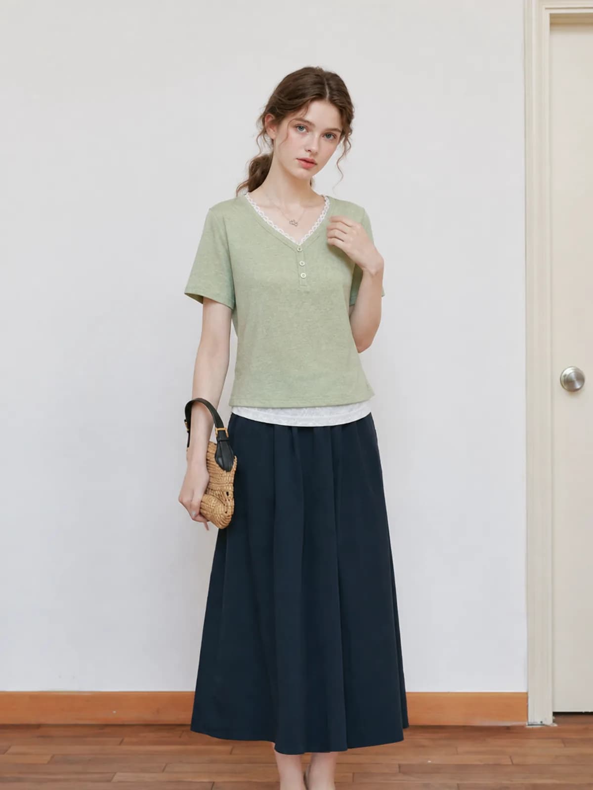 AI model in a sage green lace-trim tee and navy A-line midi skirt