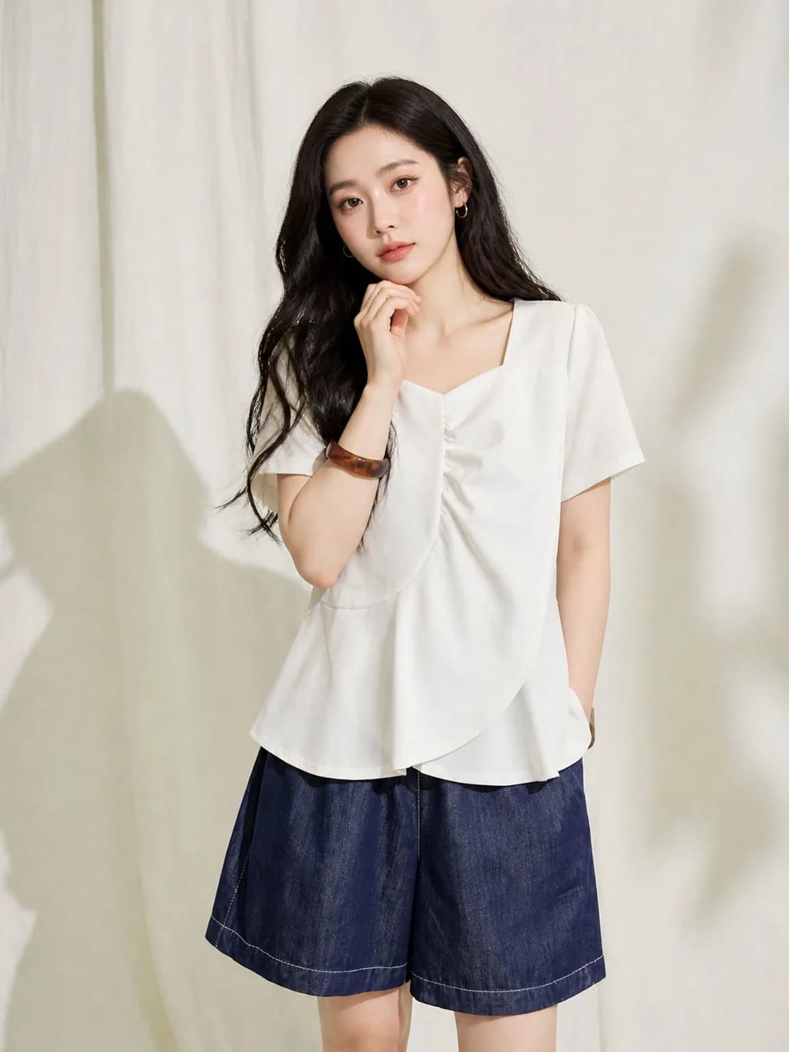 Ivory gathered-front top with navy denim shorts on a linen backdrop