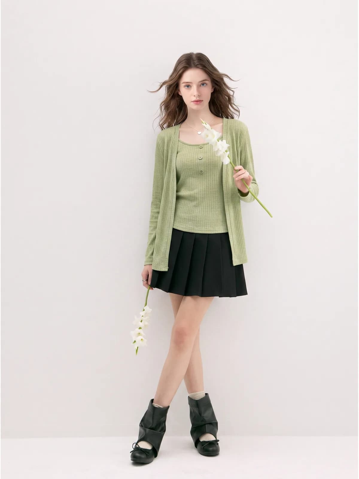 Full-length photo of a sage green cardigan and cami set with a black pleated skirt on an AI model