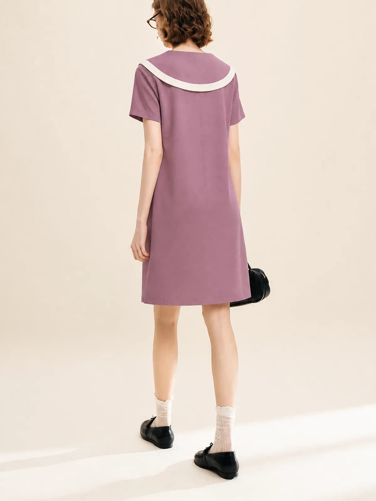 Back view of a mauve shift dress with a cream-trimmed collar on an AI model